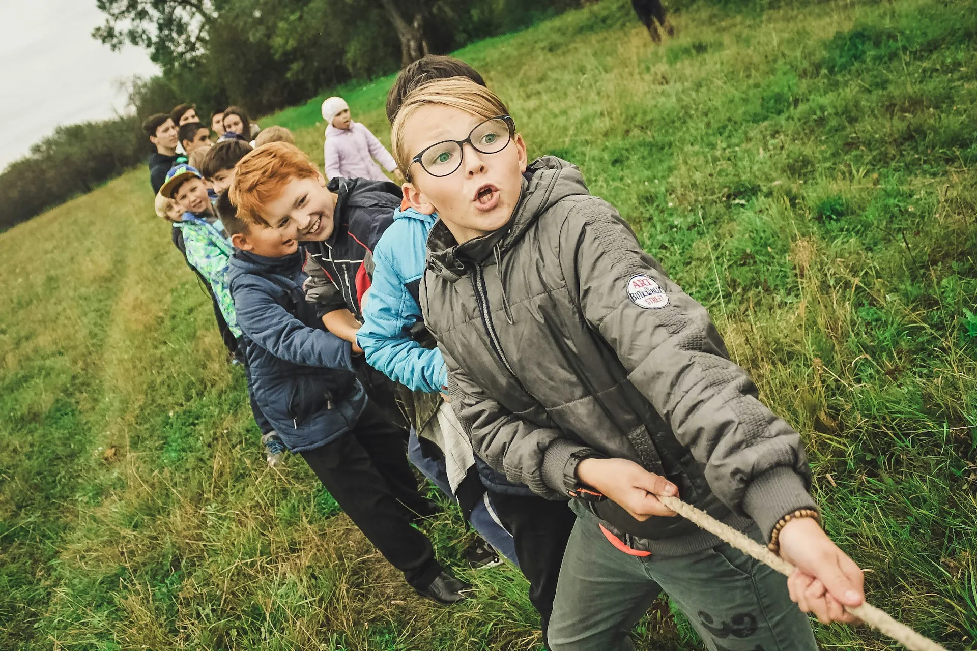Gruppo di bambini che giocano a tiro alla fune in un prato.