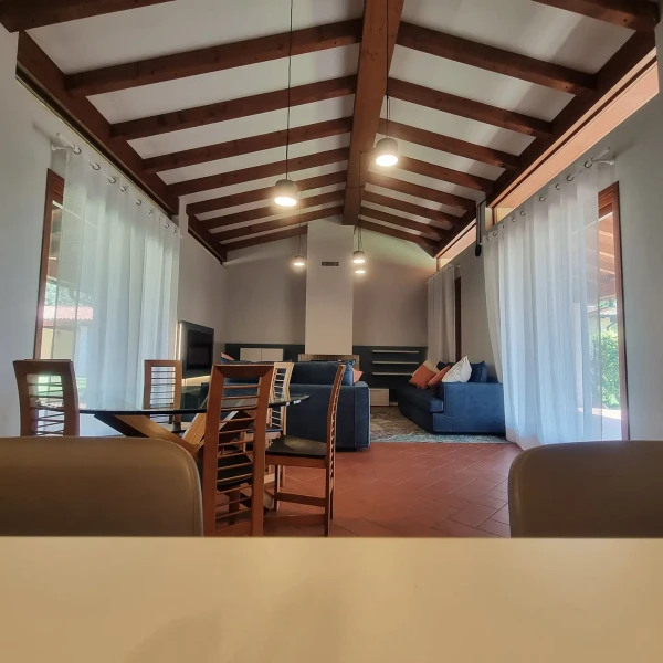 Ampio soggiorno con tetto a travi in legno, divani blu e tavolo da pranzo in vetro.