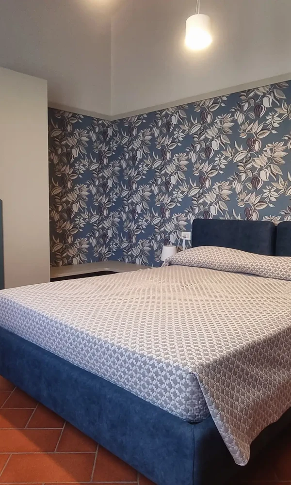 Camera da letto moderna con letto blu scuro e parete decorata con carta da parati floreale.