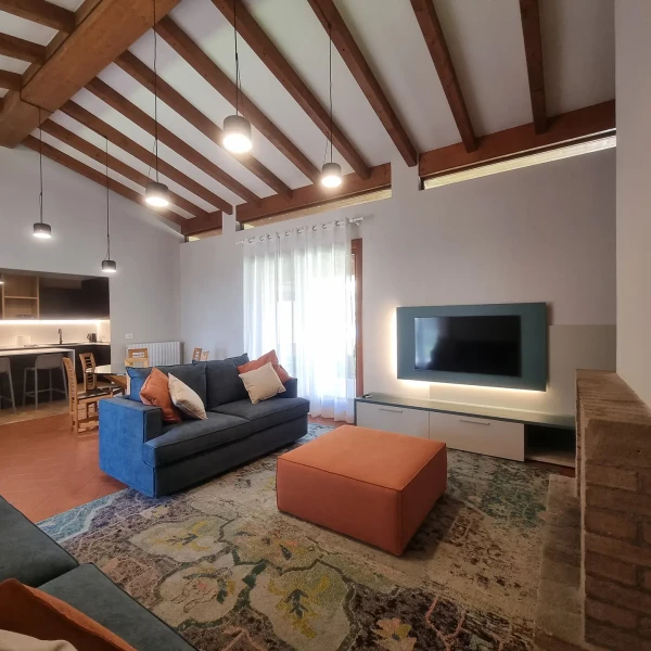 Soggiorno moderno con travi a vista, divano blu, tappeto decorato e area TV.