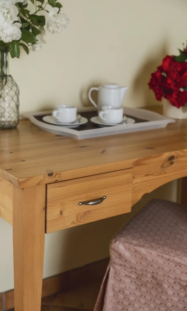 Tavolo di legno con servizio da tè, vasi di fiori bianchi e rossi e una sedia coperta da tessuto.