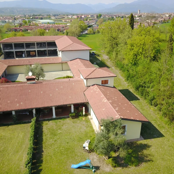 Vista aerea di un complesso con tetti in tegole rosse circondato da aree verdi e paesaggio urbano in lontananza.