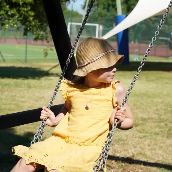 Bambina con vestito giallo e cappello seduta su un'altalena in un parco.