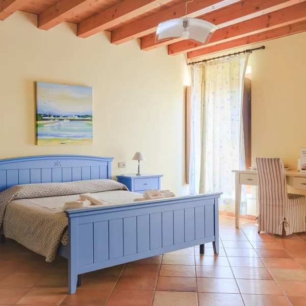 Camera da letto luminosa con letto blu, scrivania bianca e quadri alle pareti.