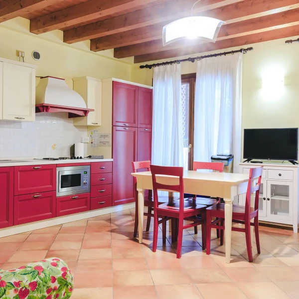 Cucina moderna con mobili rossi, tavolo da pranzo e televisore.