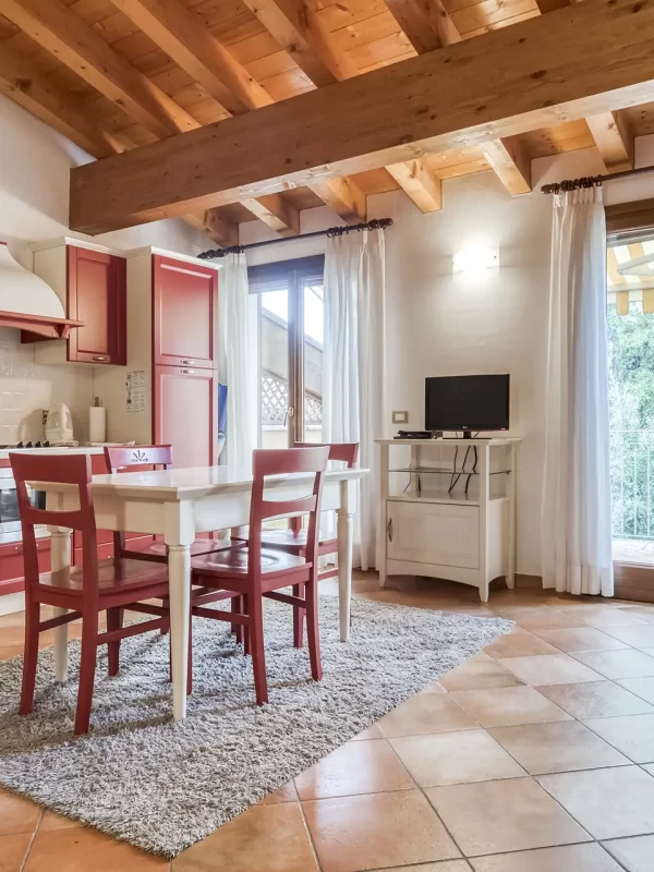 Cucina con mobili rossi e un tavolo bianco sotto un soffitto con travi in legno.