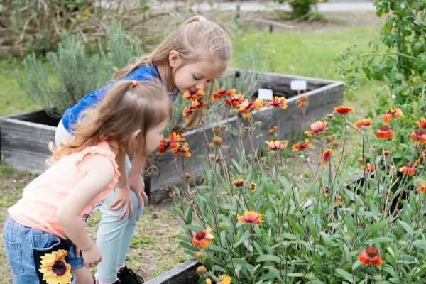 Zwei Mädchen riechen an bunten Blumen im Garten.
