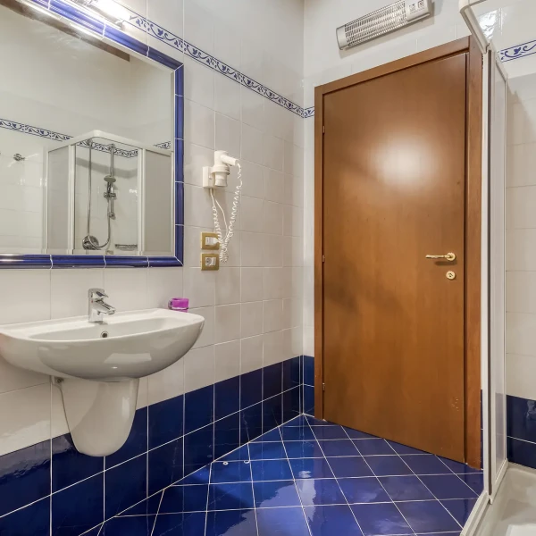 Bagno moderno con piastrelle blu, lavandino, grande specchio e box doccia.