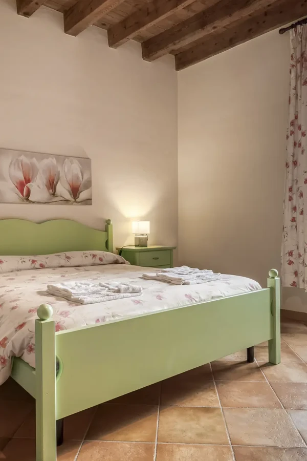 Camera da letto accogliente con letto verde, comodini coordinati e ampia finestra con vista.