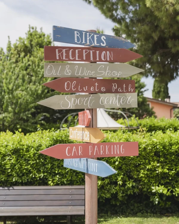 Cartello segnaletico multicolore che indica direzioni verso vari luoghi come reception, parcheggio e negozio di vino.