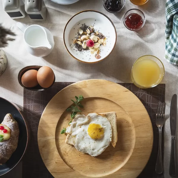 A breakfast table with toast, fried egg, croissants, juice, yogurt, and pastries.
