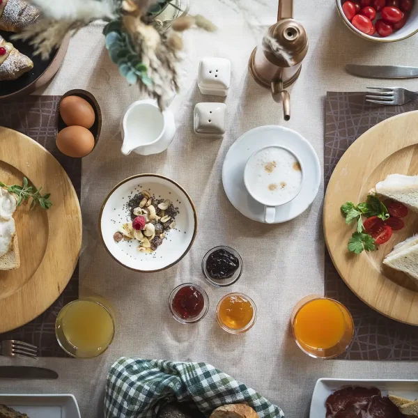 A breakfast table with toast, fried egg, sandwiches, croissants, jam, coffee, juice, and fresh vegetables.