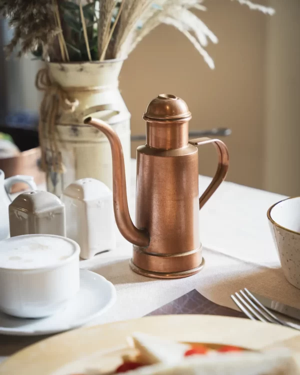 A copper kettle and a cup of coffee on a table with various tableware and decorations.
