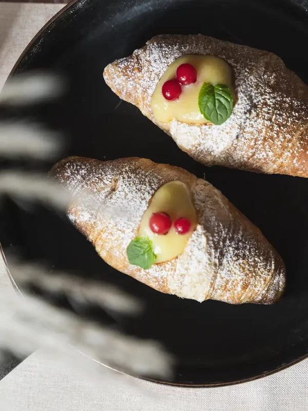 Two croissants on a black plate, topped with cream, red berries, and mint leaves.