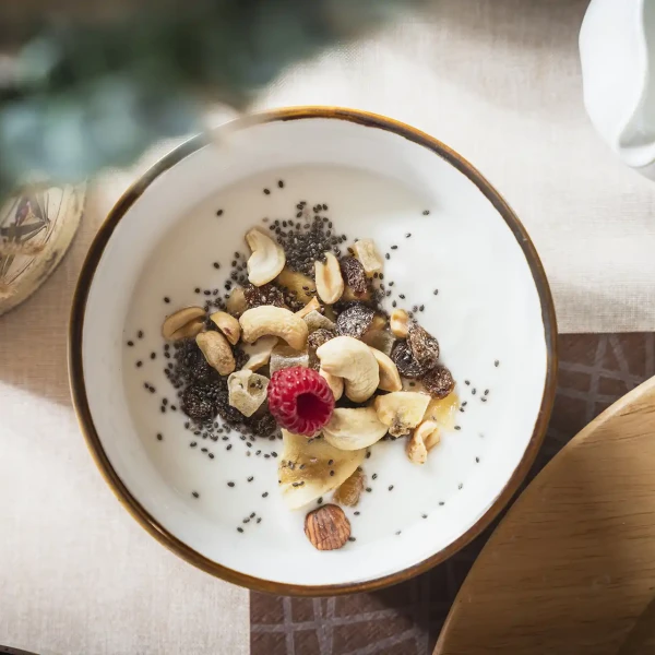 Ciotola di yogurt con frutta secca, semi di chia e una lampone al centro.