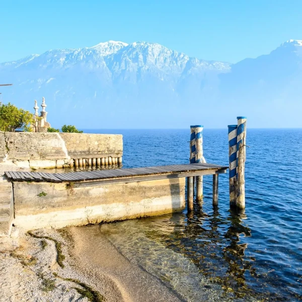 Pontile di pietra sul lago con vista sulle montagne innevate.