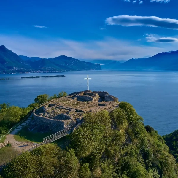 A scenic view of a cross on a hill overlooking a lake and mountains.