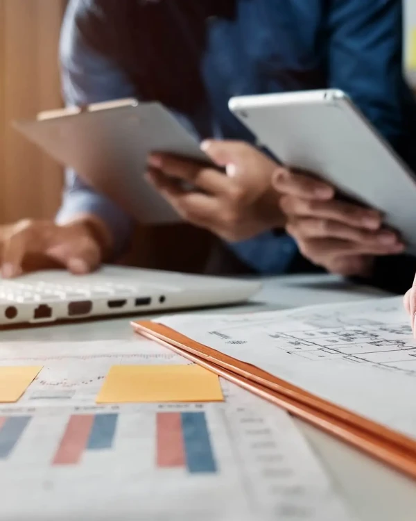 Persone al lavoro con laptop, tablet e documenti su una scrivania.