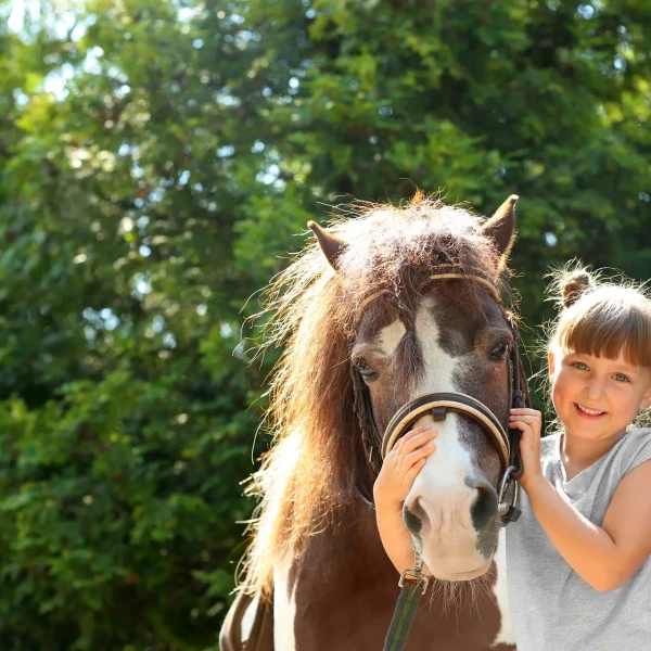 Bambina sorridente accanto a un pony, immersi nella natura.