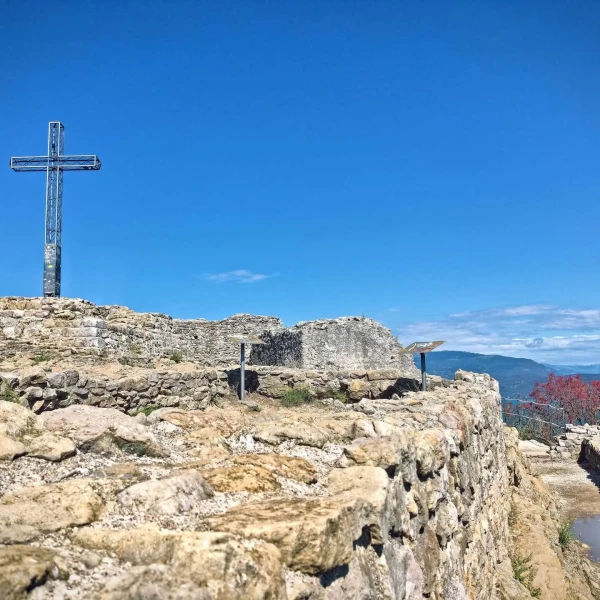 Rocky ruins with a large cross and a scenic view under a clear blue sky.