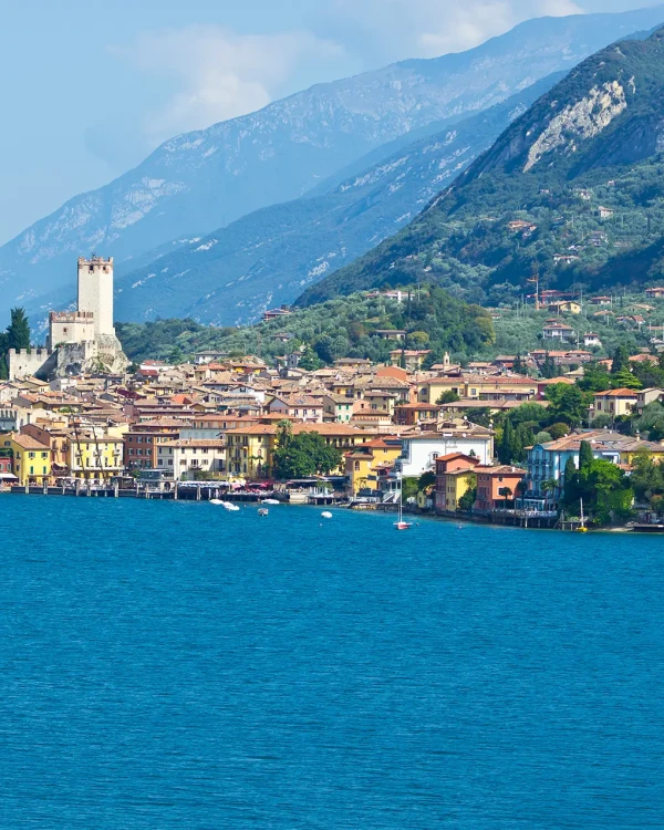 A scenic view of a lakeside town with colorful buildings and a castle surrounded by mountains.