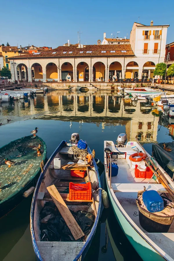 Porticciolo con barche ormeggiate e palazzi colorati riflessi nell'acqua, in un tranquillo villaggio italiano.