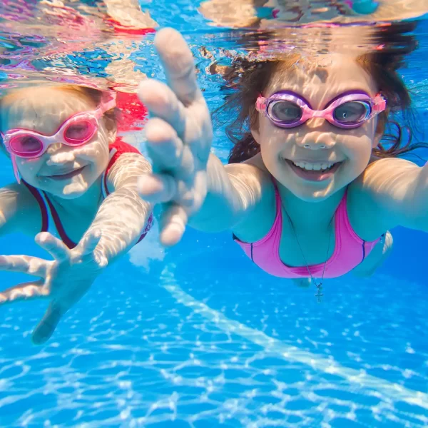 Bambine che nuotano sott'acqua con occhialini in una piscina.