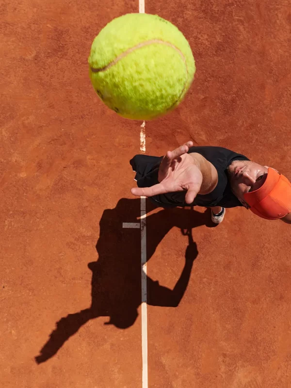 Tennisspieler beim Aufschlag auf einem Sandplatz aus der Vogelperspektive.