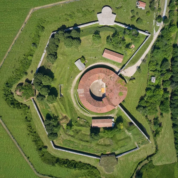 Aerial view of an octagonal fortress surrounded by green fields and trees.