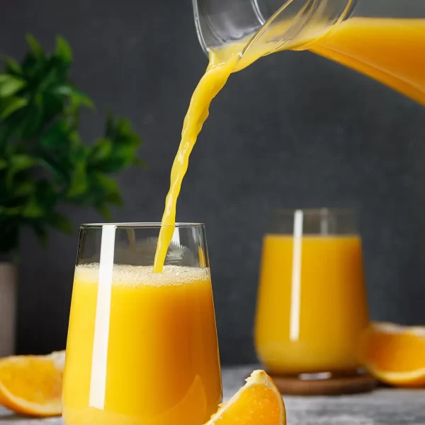 Pouring orange juice into a glass with an orange slice beside it.