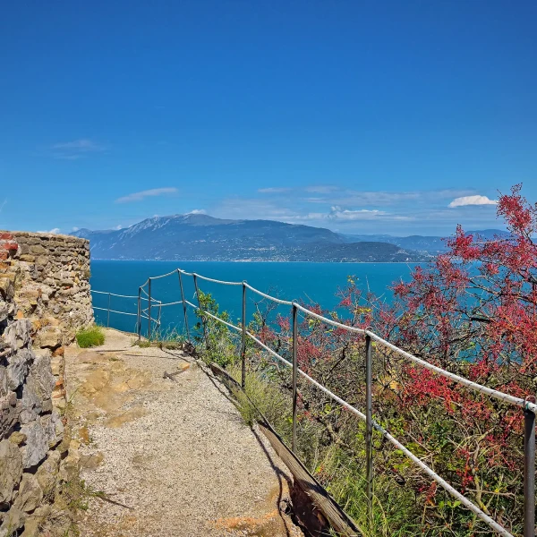 A seaside path with a stone wall, railing, and view of the ocean and mountains.