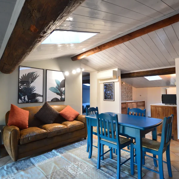 Soggiorno di mansarda arredato con divano in pelle, tavolo blu e travi a vista.