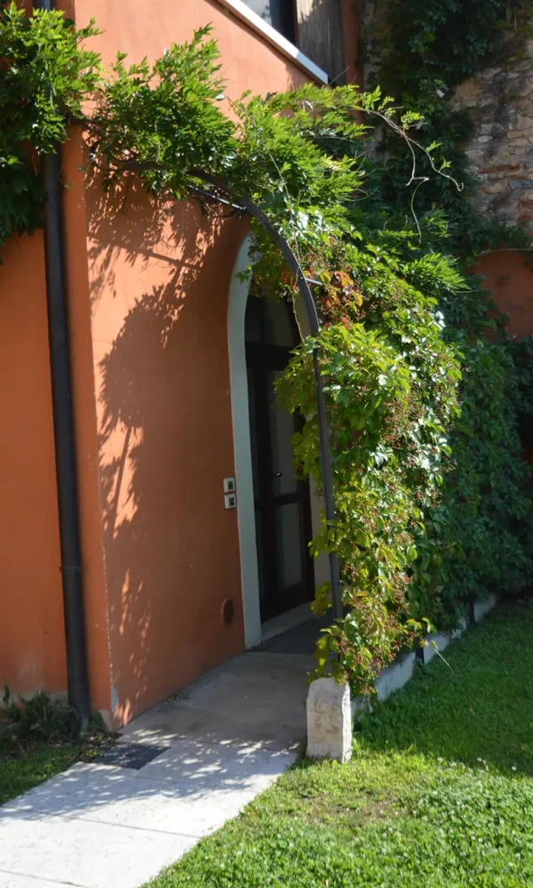 Ingresso di una casa con parete arancione e arco coperto di piante rampicanti.